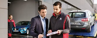 Service- und Werkstattmitarbeiter besprechen ein Dokument vor dem Autohaus(SEAT)
