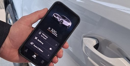 Eine Hand hält ein Smartphone vor einem Auto. Auf dem Smartphone sind Inhalte der Connect App abgebildet, zum Beispiel aktuelle Tankfüllung. (Ratio Mobil)